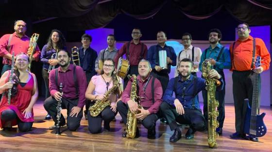 Los miembros de la Banda de Conciertos de Limón posan con sus instrumentos dentro de un escenario. Todos visten de colores vistosos y sonríen a la cámara.