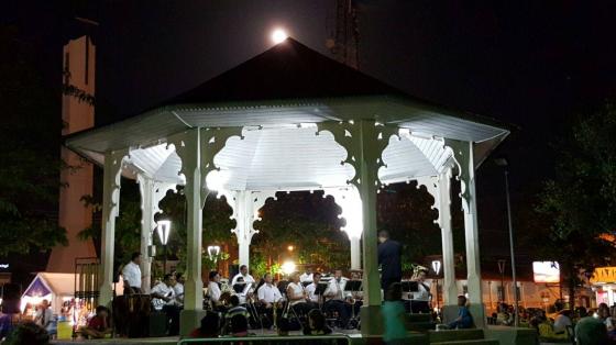 Músicos de la Banda de Conciertos de Guanacaste tocando dentro del kiosco de Liberia en la noche, con luz interna del kiosco que ilumina de manera especial al ensamble y sus instrumentos.