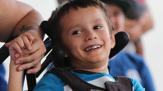 Niño en silla de ruedas muy sonriente tomado de la mano de su madre