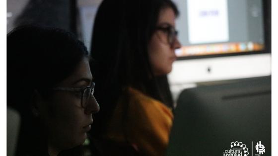 Dos jóvenes prestando atención a una clase, detrás de ellas varias computadoras