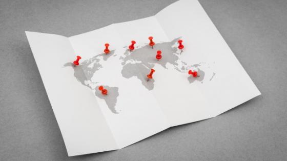Mapa mundi en una hoja de papel con clips señalando diversos lugares