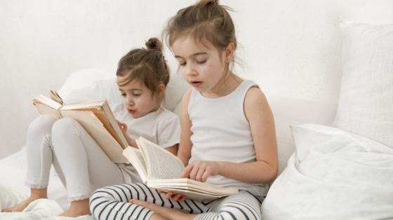 Dos niñas pequeñas leyendo un libro en la cama