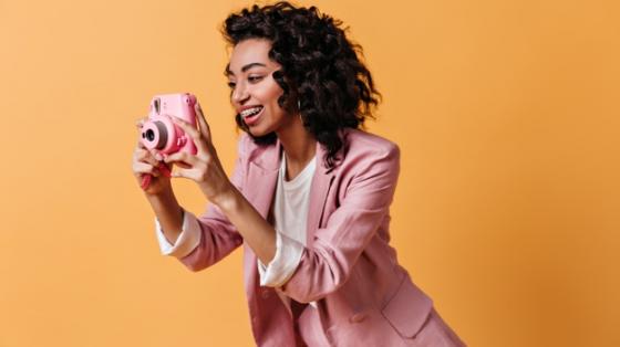 Mujer sonriente con chaqueta rosa, tomando una fotografía