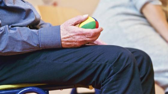 Persona adulto mayor sosteniendo con su mano una bola pequeña de colores. 