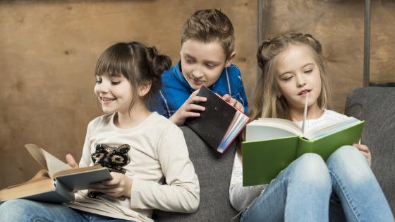 Dos niñas y un niño leyendo sentados en un sillón.