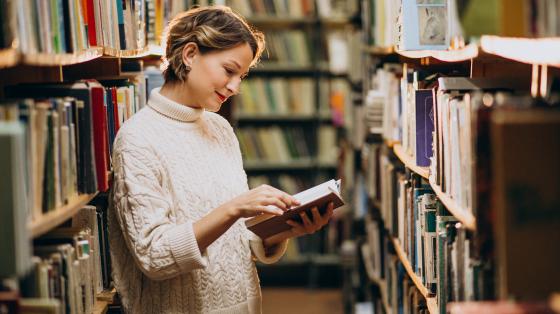 Mujer leyendo en la biblioteca entre la estantería.