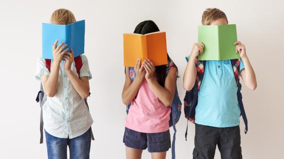 Niños y niña leyendo libros de pie. 