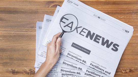 Persona con lupa revisando un papel periódico con las letras "fake news".