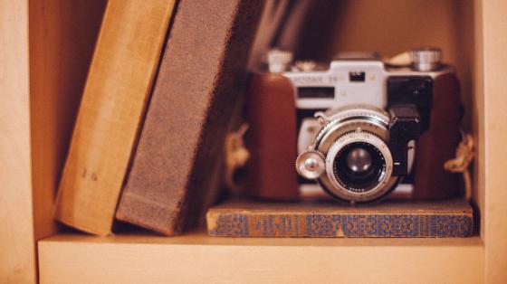 Fotografía de una cámara fotográfica colocada al lado de dos libros de color café.