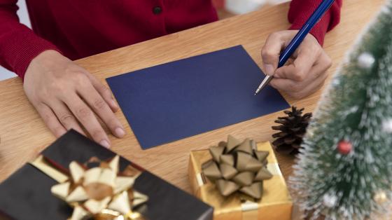 Manos tomando un lapicero sobre una hoja azul en una mesa de madera con adornos navideños. 