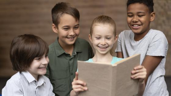 Taller para niños y niñas "Hagamos un libro" Grupo de niños leyendo del mismo libro.