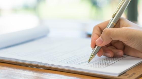 Sobre una mesa de madera un persona escribiendo en una hoja de papel.