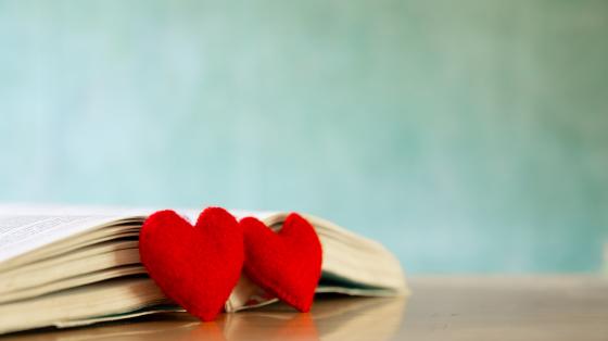 Fondo turquesa claro. Un libro abierto sobre una mesa y al lado dos corazones de peluche.