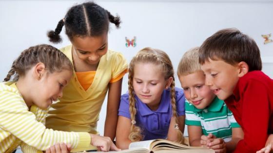 Imagen grupo de niños reunidos en torno a un libro abierto viendo con interés el contenido.