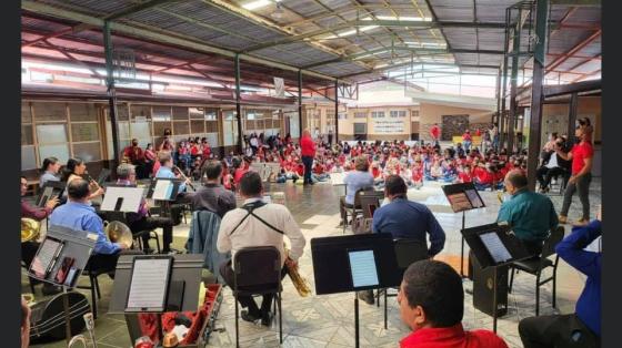 Foto de la Banda con niñas y niños al fondo disfrutando el Concierto Didáctico