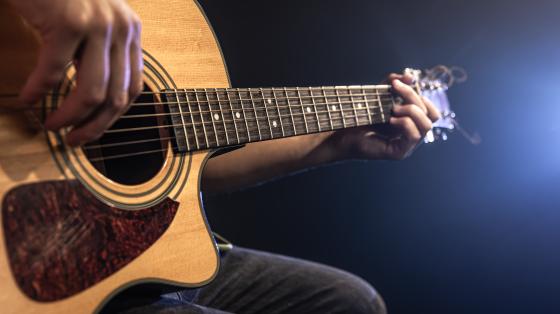 En primer plano, persona tocando guitarra acústica.