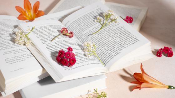 Sobre una mesa blanca, tres libros apilados y abiertos entre diversas flores y pétalos.