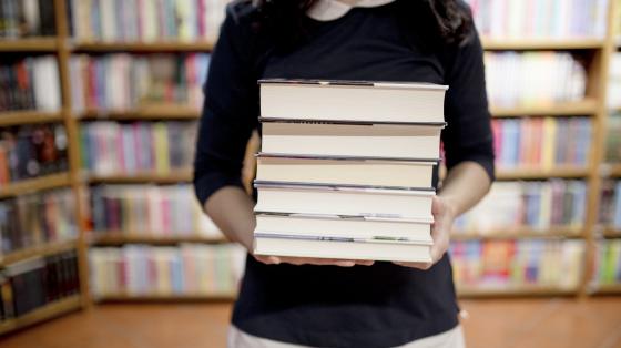 Recital "Llorar, reír, vivir" con escritoras de Palabras Viajeras Mujer sosteniendo una pila de libros.