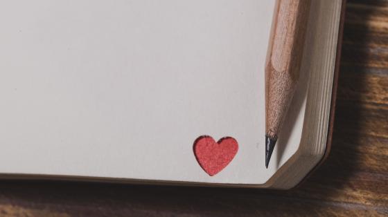 Fondo de madera. Esquina de un libro con un corazón rojo y un lápiz de grafito a la derecha. 