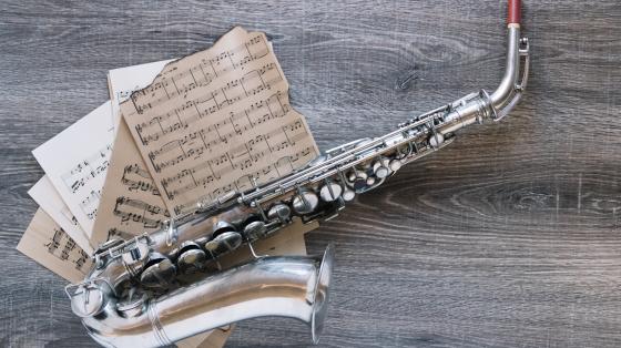Fondo de madera. Un saxofón sobre partituras musicales. 