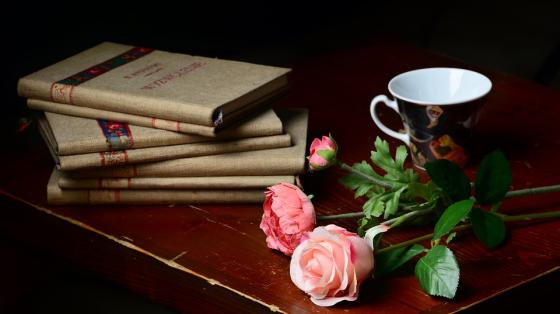 Sobre un escritorio de madera unos libros, una taza y unas flores