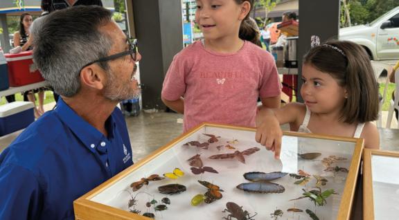 Caja con varias Mariposas y se las muestrasn a dos niños un funcionario del Museo Nacional de Costa Rica