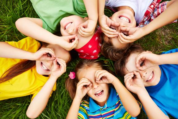 Fotografía de cinco niños acostados en zacate sonriendo.