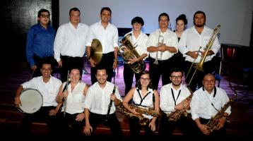 La Banda de Conciertos de Limón posando en un escenario vestidos de blanco y negro sonríen sosteniendo sus instrumentos entre las manos.