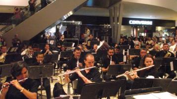 Músicos de la Banda de Conciertos de Cartago tocando en una sala de un mall rodeados de mucho público.