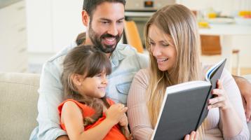 Padres leyendo con su hija en la sala de una casa. 