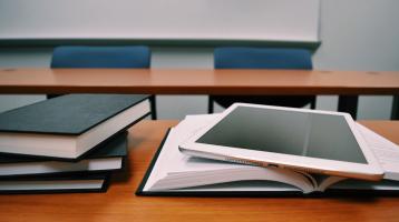 Libros apilados y una tableta sobre un libro abierto en un salón de clase. 