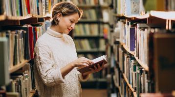 Mujer leyendo en la biblioteca entre la estantería.