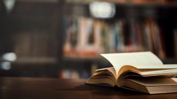 Libro abierto por la mitad sobre una mesa y de fondo una biblioteca.