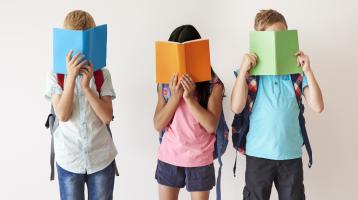 Niños y niña leyendo libros de pie. 