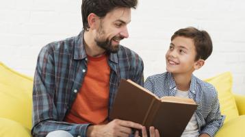 Padre sosteniendo un libro y mirando a su hijo.