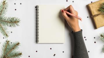 Mano escribiendo en una libreta en un fondo navideño