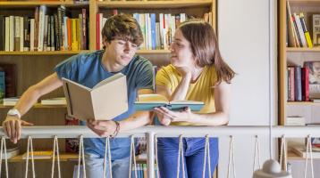 Dos jóvenes leyendo en la biblioteca.