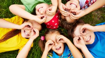 Fotografía de cinco niños acostados en zacate sonriendo.