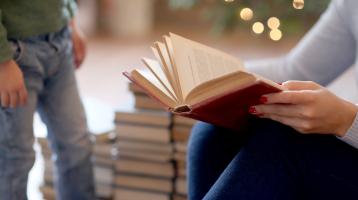 Persona sosteniendo un libro abierto y a la izquierda un niño. Fondo navideño. 