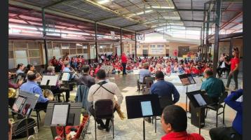 Foto de la Banda con niñas y niños al fondo disfrutando el Concierto Didáctico