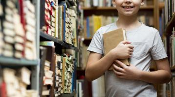 Un niño sosteniendo un libro en medio de una colección de libros.