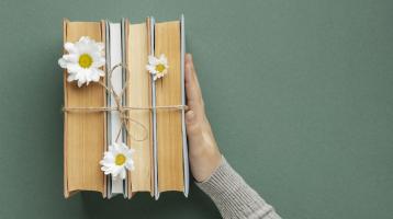 Fondo gris. Desde vista superior unos libros decorados con flores y una mano los sostiene.